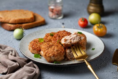 Gri tabakta et, çatalda bir dilim, gri bir masa, domateslerin yanında yeşillikler.