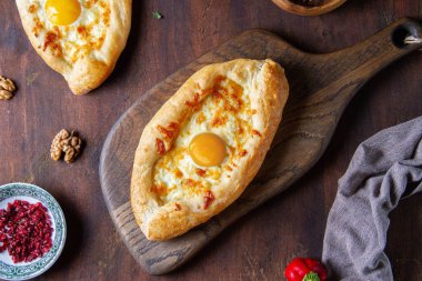 Tahta kahverengi bir masada peynirli ve yumurtalı Gürcü tekneleri.