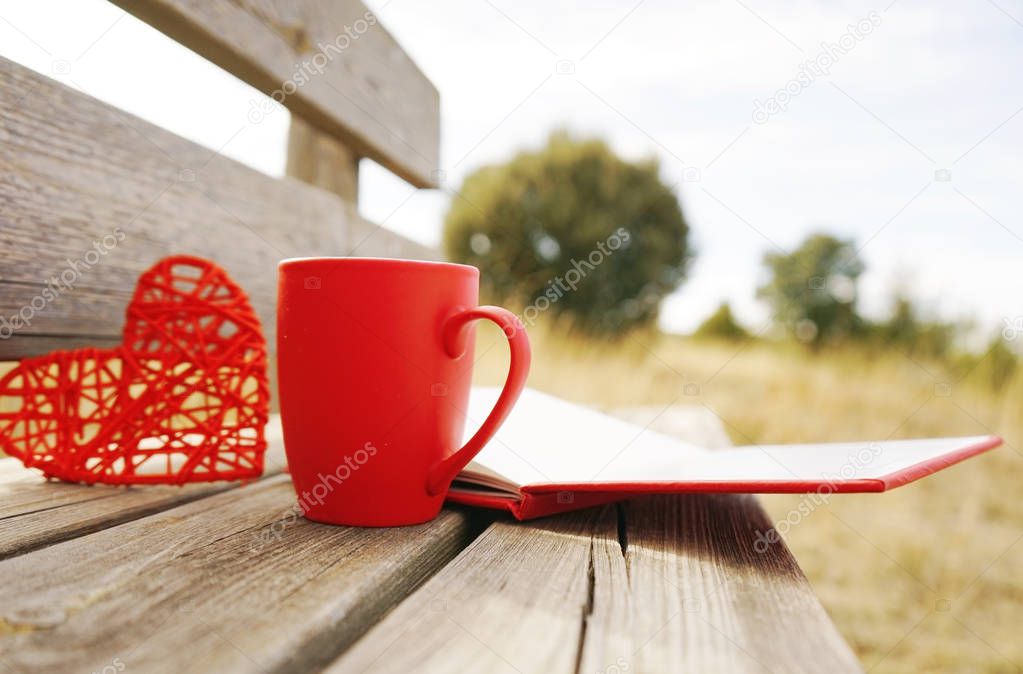 Red mug with coffee and open book on wooden bench