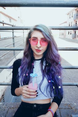 Mutlu güzel teen pembe güneş gözlüğü ile içecekler ve kentsel yerde oturan bir pembe içecek sahiptir
