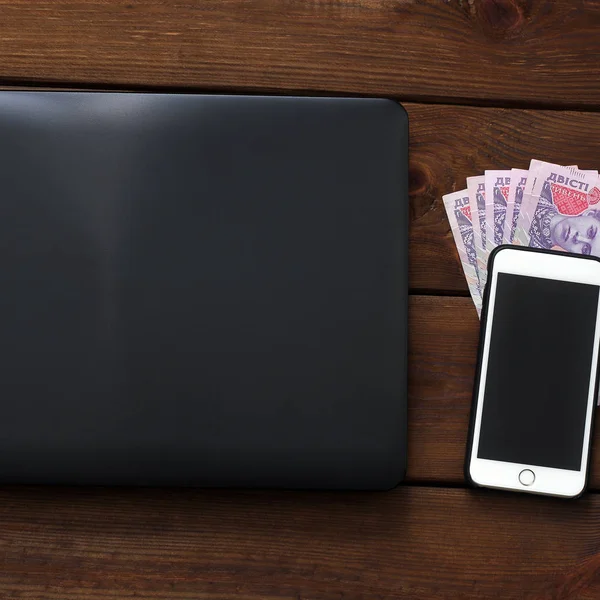 Laptop, telefon i pieniądze na podłoże drewniane. Technika i ukraińskich pieniądze — Zdjęcie stockowe