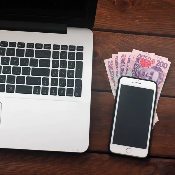 Laptop, phone and money on wooden background. Technique and Ukrainian money