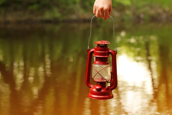 Kerosene lamp in hand against the background of the river