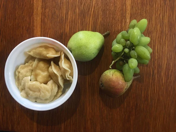 Essen auf einem Holztisch. Knödel im Teller. Trauben und Birnen — Stockfoto