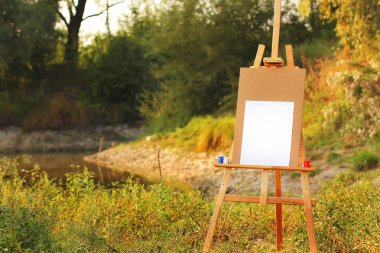 Doğanın arka planında boyalar olan Easel.