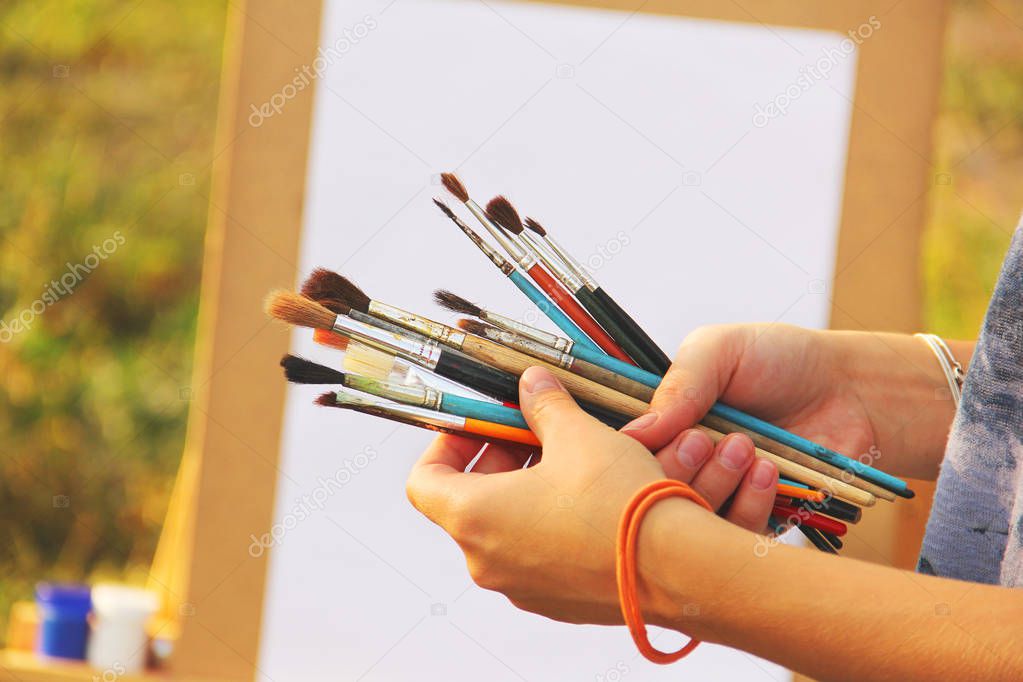 Paint brushes in hand on the background of an easel with paints
