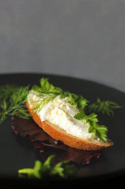 Süzme peynirli sandviç ve siyah tabakta otlar. Ev yapımı süzme peynir. Atıştırmalık Kullanılacak siyah gereçler