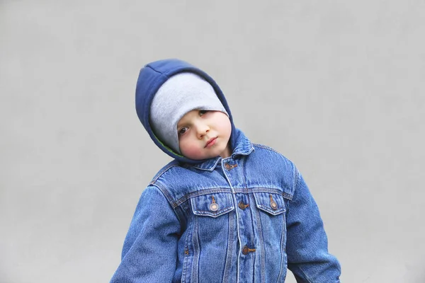 一个穿着夹克和帽子的男孩正在看着摄像机 一个灰色背景的时髦孩子 穿斜纹棉布夹克的那个 — 图库照片