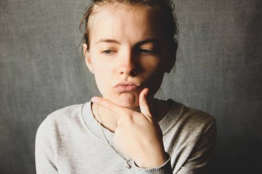 Kız gri bir arka planda düşünüyor. Duygusal bir kız. Yüz duyguları.