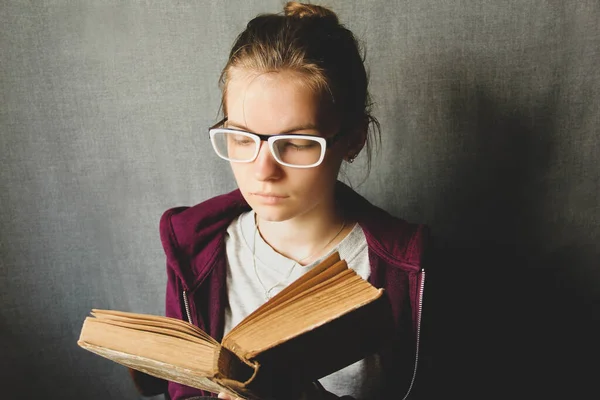 Girl with glasses reads a book. The girl is holding an old book.