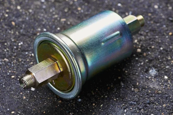 A new fuel filter enclosed in a metal casing with an inlet and outlet on fuel lines on a dark background