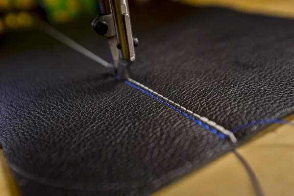 Black leather on industrial sewing machine with white and blue stitches