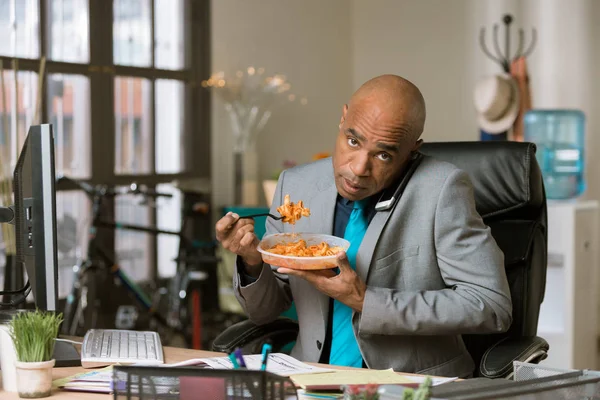 Hombre en el teléfono y comiendo en su escritorio — Foto de Stock