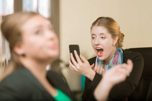 Mulher aplicando maquiagem usando seu telefone como um espelho — Fotografia de Stock