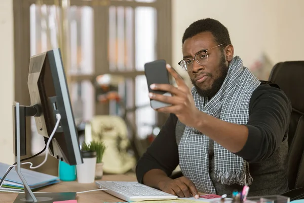 Sceptyczny człowiek w biurze za pomocą urządzenia mobilnego — Zdjęcie stockowe