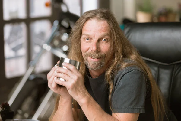 Mann an seinem Schreibtisch mit Kaffee und Motorrad im Hintergrund — Stockfoto
