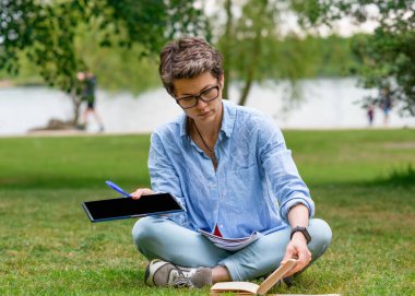  Yeşil çimenlerde oturan ve tablette çalışan bir kadın.