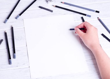 Mockup for a drawing. Hands drawing by compressed charcoal. A few pencils and black compressed charcoal. View from above.