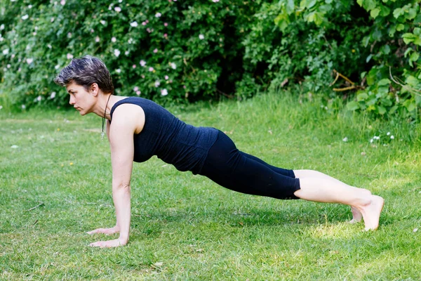 International day of yoga. Woman doing yoga outside on green grass on sunny warm day in park