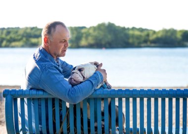 Adam ve İngiliz bulldog göle karşı parkta yürüyüşe çıkıyorlar.