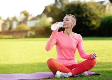Kadın çimenlerde egzersiz yaptıktan sonra su içiyor.