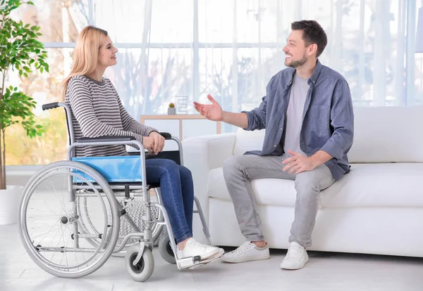 Young man talking with woman in wheelchair indoors