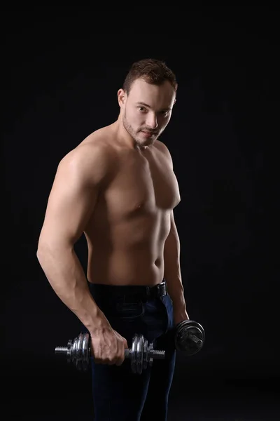 Gespierde jonge bodybuilder met dumb-bells op donkere achtergrond — Stockfoto
