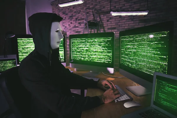 Masked hacker in room with computers — Stock Photo, Image