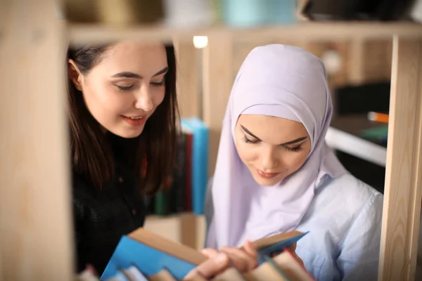 Vrouwelijke student en haar islamitische klasgenoot in bibliotheek — Stockfoto