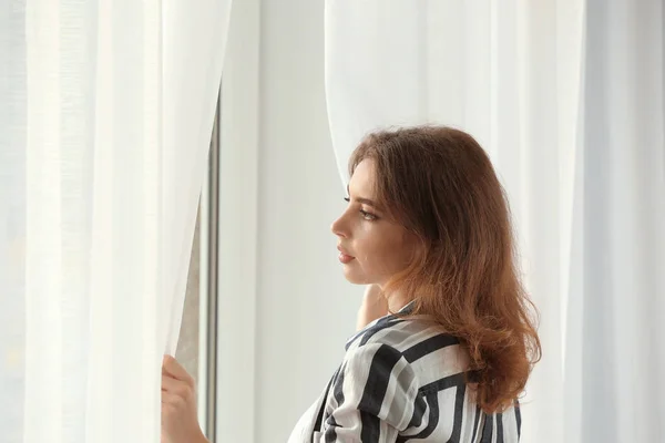 Jeune femme ouvrant rideaux à l'intérieur — Photo