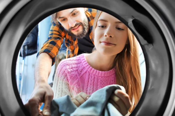 Pareja haciendo la colada en la lavandería, vista desde el interior de la lavadora — Foto de Stock