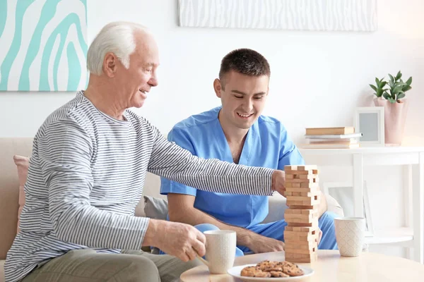 Hombre mayor jugando juego de mesa con su cuidador en casa —  Fotos de Stock