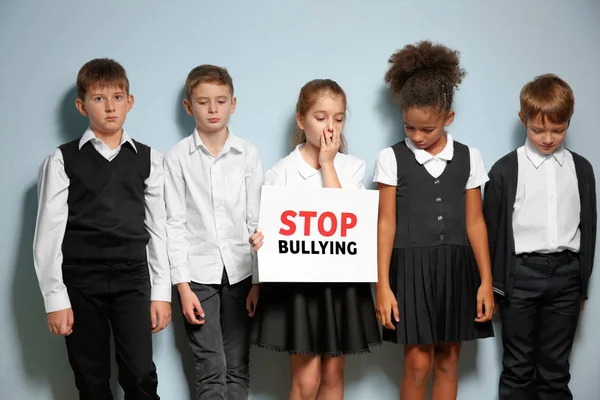 Niños pequeños con uniforme escolar sosteniendo el letrero "Stop bullying" sobre fondo claro —  Fotos de Stock