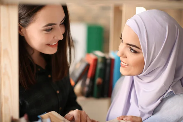 Female student and her Muslim classmate in library — Stock Photo, Image