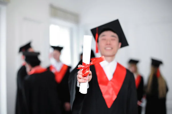 Nöjd student i bachelor mantel med diplom inomhus. Graduation dagen — Stockfoto