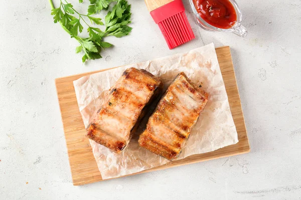 Tablero de madera con deliciosas costillas a la parrilla en la mesa —  Fotos de Stock