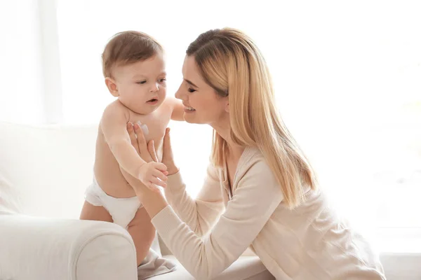 Mulher aplicando creme corporal em seu bebê dentro de casa — Fotografia de Stock