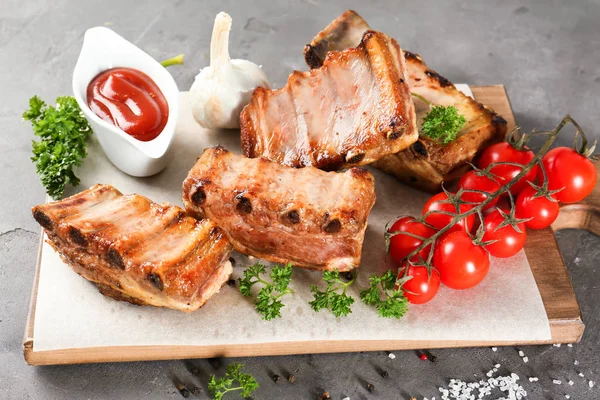 Placa de madeira com deliciosas costelas grelhadas, tomates e molho na mesa — Fotografia de Stock