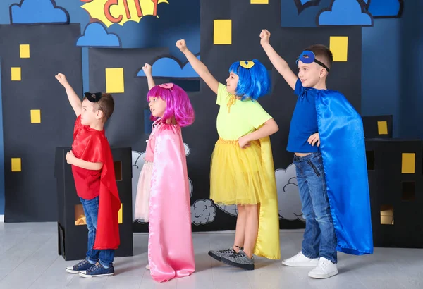 Cute children in superhero costumes against comic strip themed decoration