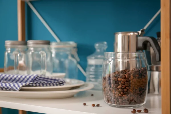 Glass jar with coffee beans on shelf of storage unit indoors