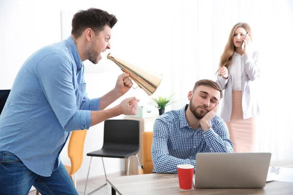 Angry boss with megaphone screaming at sleeping employee in office