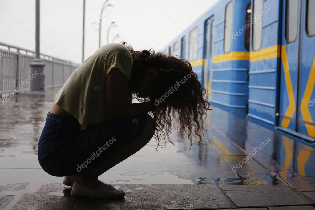 Depressed young woman at railway station on rainy day