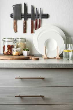 Kitchen counter with glass jars, knives and set of white plates clipart