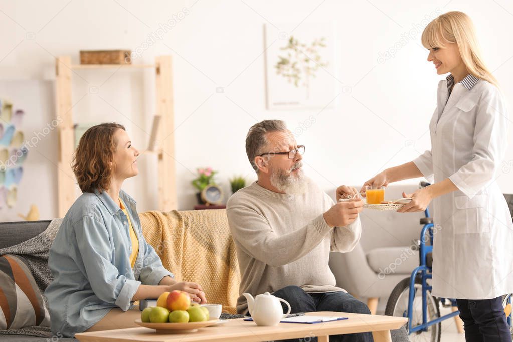Young caregiver with senior man and his daughter at home