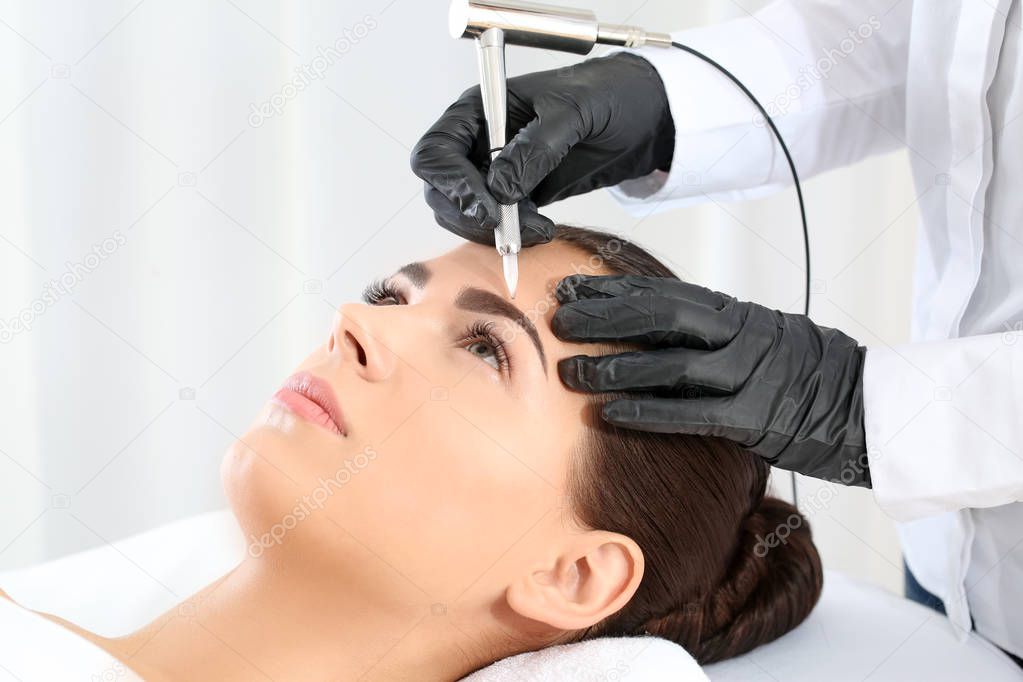 Young woman undergoing procedure of eyebrow permanent makeup in beauty salon