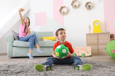 Little boy playing with ball at home while his nanny is taking selfie clipart