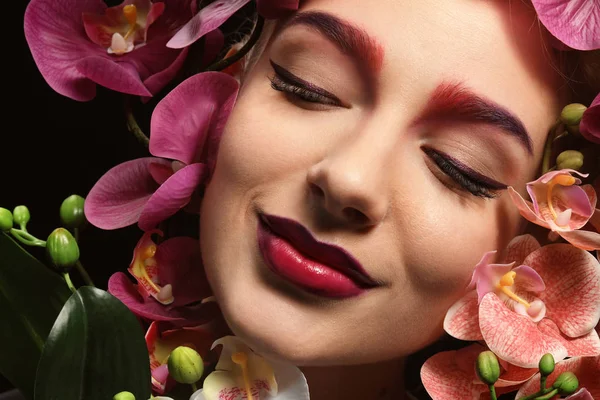 Jonge vrouw met geverfd wenkbrauwen omringd door bloemen — Stockfoto