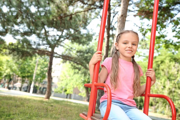 Schattig klein meisje spelen op schommels in park — Stockfoto