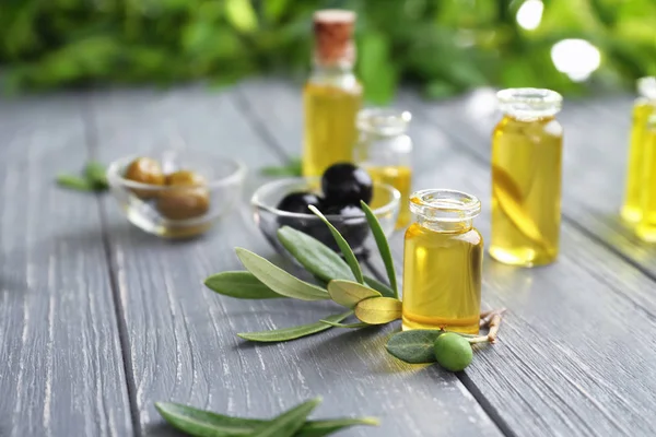 Samenstelling van olijven in kom en flessen met olieverf op houten tafel — Stockfoto