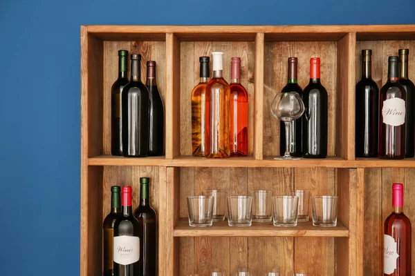 Wooden storage stand with wine bottles and glasses indoors — Stock Photo, Image